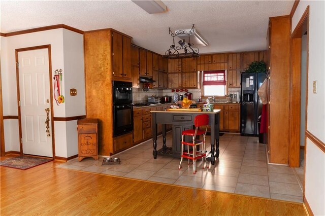 kitchen featuring light wood-type flooring, under cabinet range hood, black appliances, and brown cabinets