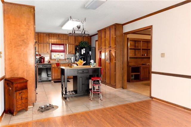 kitchen featuring crown molding, baseboards, brown cabinets, light wood-style floors, and black appliances