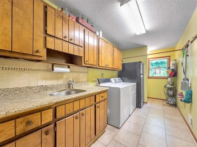 washroom with light tile patterned floors, baseboards, a textured ceiling, a sink, and washing machine and dryer