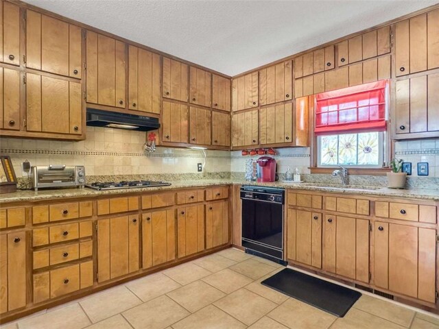 kitchen with under cabinet range hood, a toaster, a sink, stainless steel gas stovetop, and black dishwasher