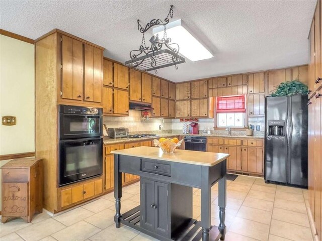 kitchen with light countertops, a chandelier, brown cabinetry, under cabinet range hood, and black appliances