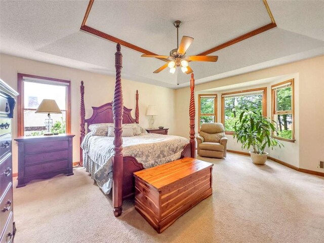 bedroom with a textured ceiling, baseboards, a ceiling fan, a tray ceiling, and light colored carpet