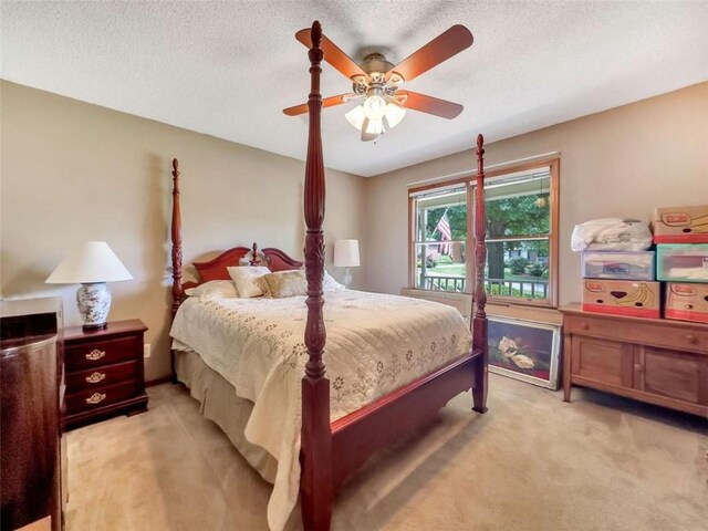 bedroom featuring light colored carpet, a ceiling fan, and a textured ceiling