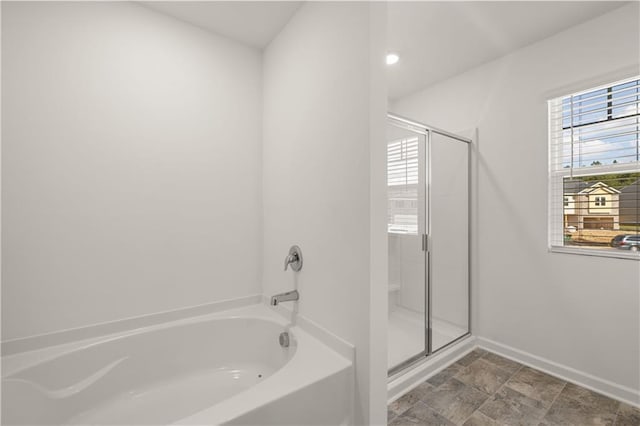 full bathroom featuring a shower stall, a garden tub, baseboards, and stone finish floors