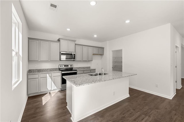 kitchen featuring appliances with stainless steel finishes, gray cabinetry, a sink, a center island with sink, and baseboards