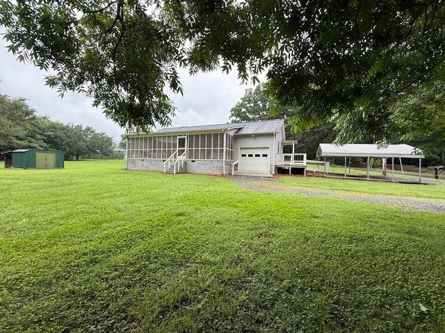 100 Walter Leon Dr, Chatsworth, GA 30705 - back of house featuring a sunroom, an attached garage, a lawn, a storage unit, and a carport