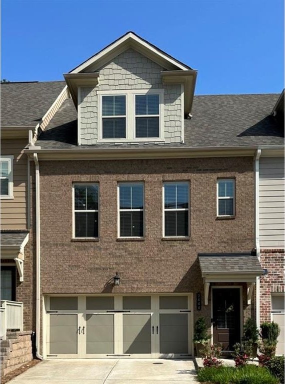 view of property featuring a garage, a shingled roof, driveway, and brick siding