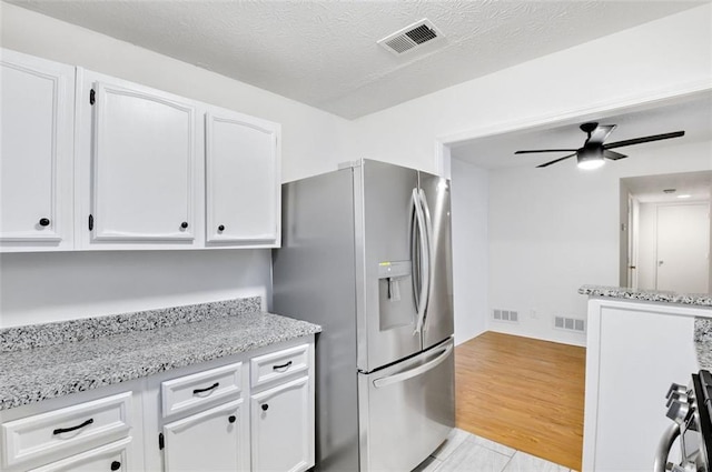 kitchen featuring white cabinetry, stainless steel appliances, light stone countertops, a textured ceiling, and light wood-type flooring