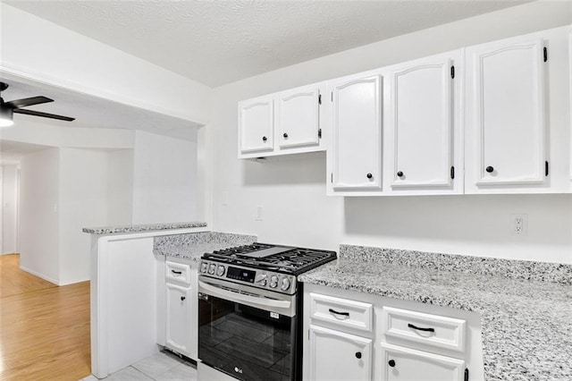 kitchen with gas range, a textured ceiling, light stone counters, and white cabinets