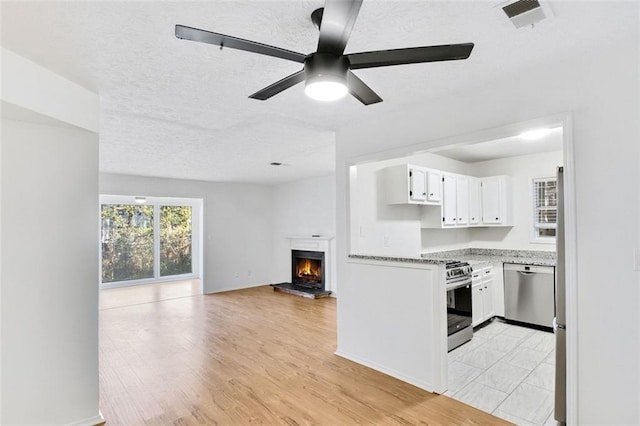 kitchen featuring ceiling fan, stainless steel appliances, light stone countertops, and white cabinets