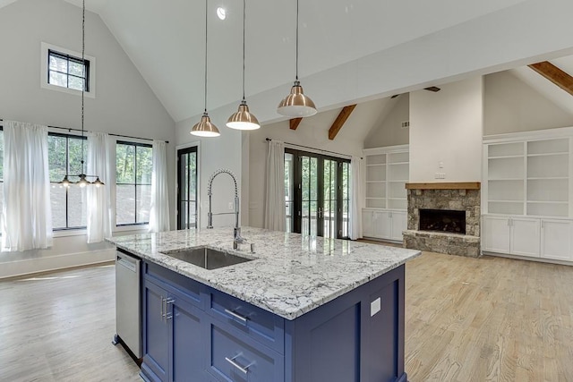 kitchen featuring blue cabinetry, stainless steel dishwasher, a sink, a stone fireplace, and light wood-type flooring