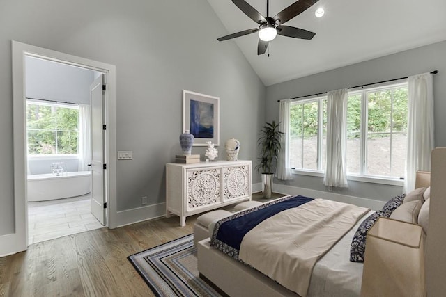 bedroom with connected bathroom, multiple windows, high vaulted ceiling, and wood finished floors