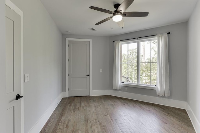 empty room featuring a ceiling fan, baseboards, visible vents, and wood finished floors