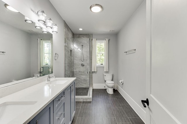 bathroom with double vanity, baseboards, toilet, a shower stall, and a sink