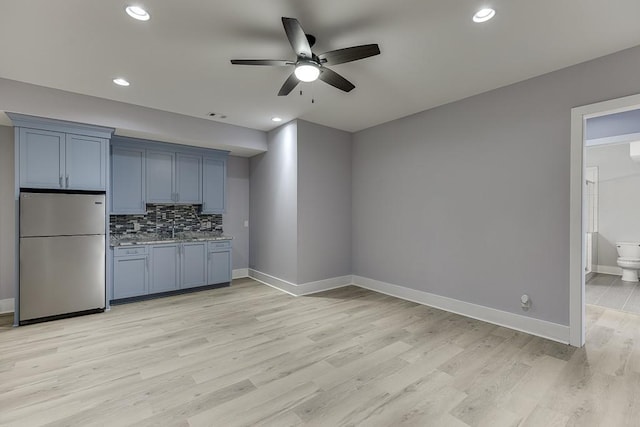 kitchen featuring ceiling fan, baseboards, light wood-type flooring, freestanding refrigerator, and tasteful backsplash