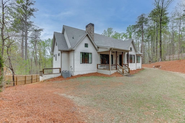 back of property with a porch, central air condition unit, a shingled roof, fence, and a chimney