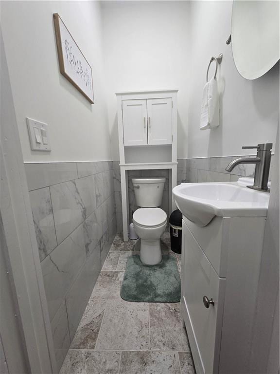 bathroom featuring a wainscoted wall, tile walls, and toilet