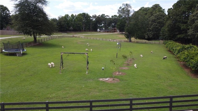 view of property's community featuring a rural view, a trampoline, fence, and a lawn