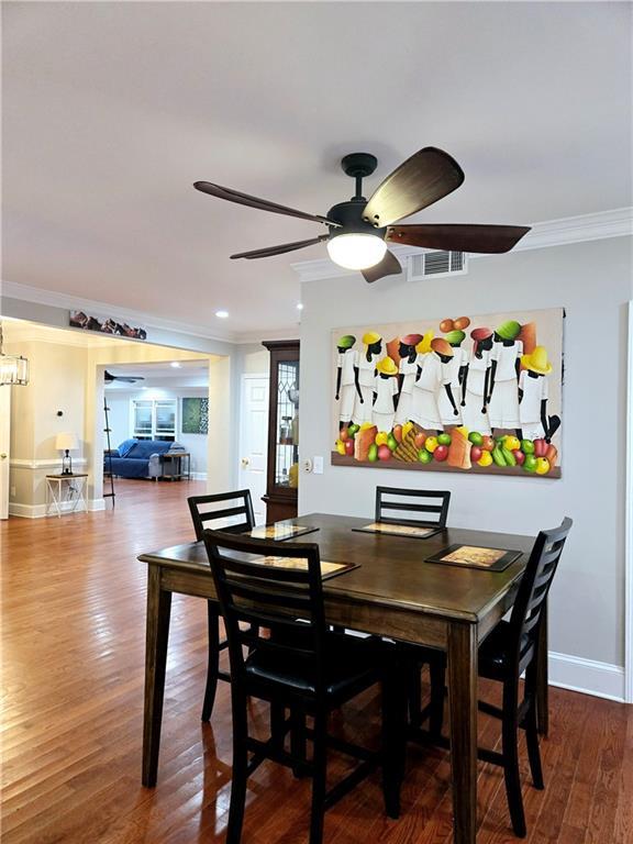 dining room with crown molding, visible vents, a ceiling fan, wood finished floors, and baseboards