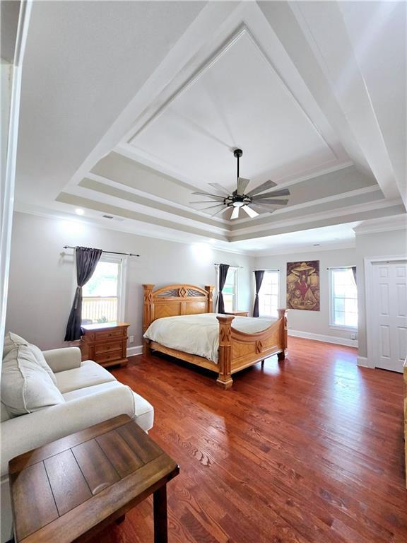 bedroom with ceiling fan, wood finished floors, baseboards, a tray ceiling, and crown molding