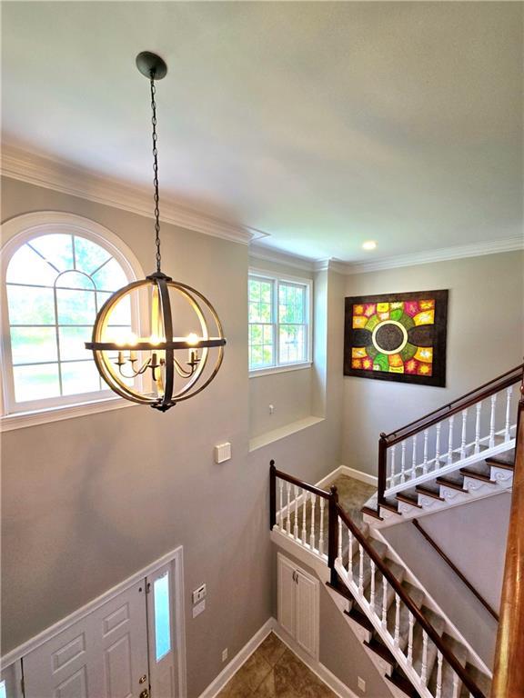 stairs featuring plenty of natural light, tile patterned flooring, ornamental molding, and an inviting chandelier