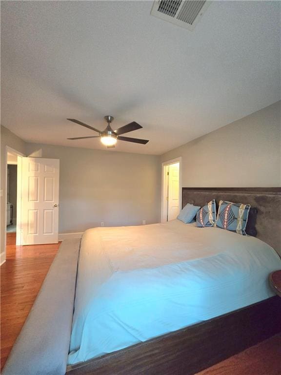 bedroom with a ceiling fan, baseboards, visible vents, and wood finished floors