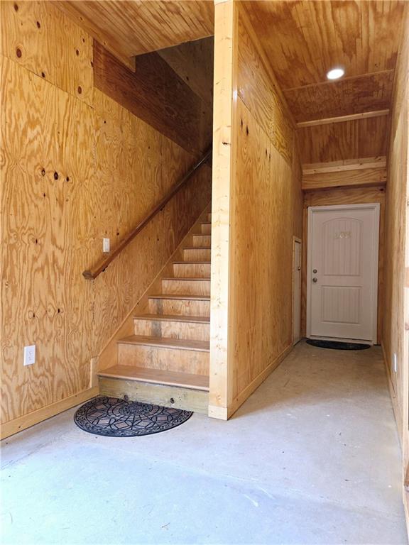 stairs featuring concrete floors, wooden walls, and wood ceiling