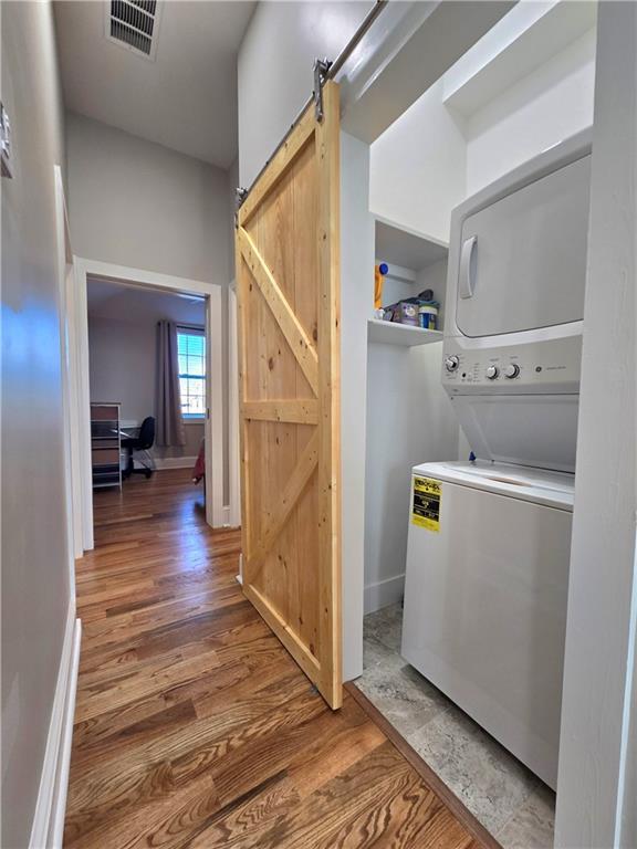 washroom featuring hardwood / wood-style flooring, a barn door, and stacked washing maching and dryer