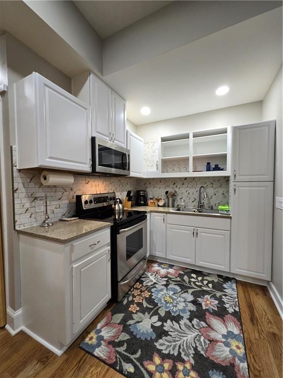 kitchen featuring wood finished floors, appliances with stainless steel finishes, a sink, and tasteful backsplash