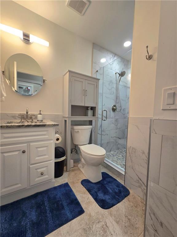 full bathroom featuring a marble finish shower, visible vents, toilet, a wainscoted wall, and tile walls