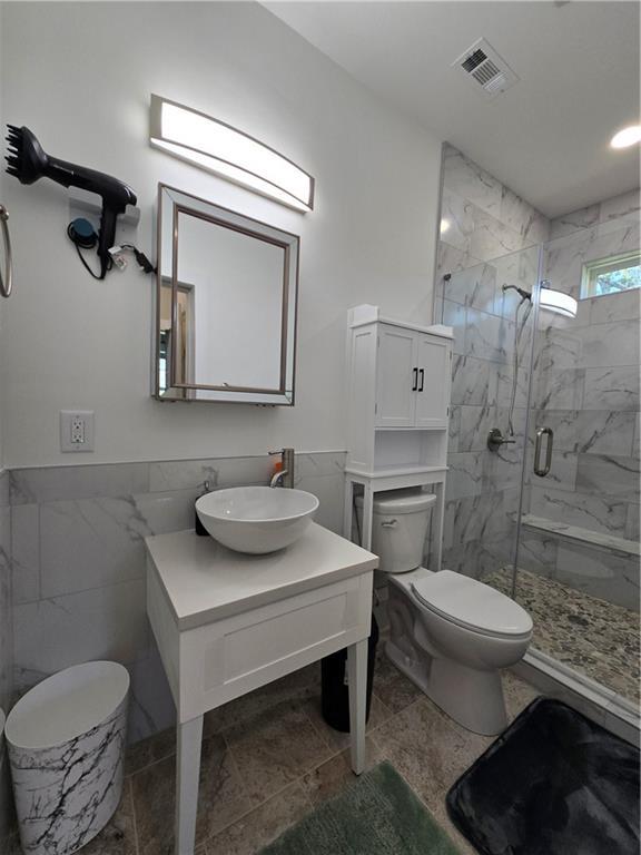 bathroom with toilet, vanity, visible vents, tile walls, and a marble finish shower