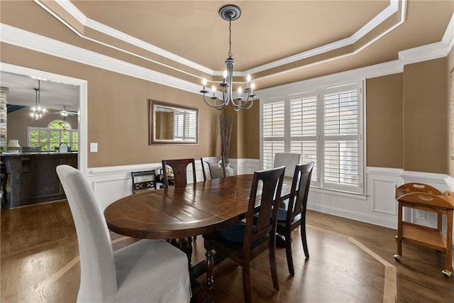 dining area with a raised ceiling, a wainscoted wall, an inviting chandelier, ornamental molding, and dark wood-type flooring
