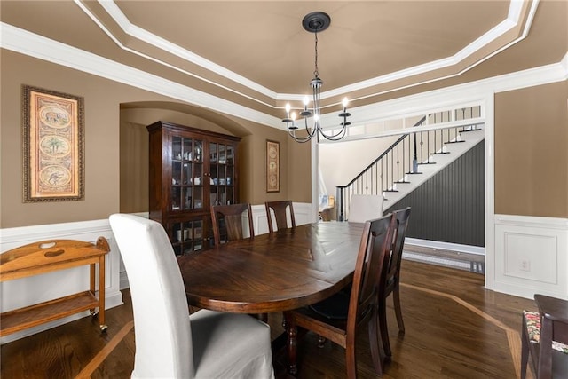dining area featuring a raised ceiling, ornamental molding, wood finished floors, and a chandelier