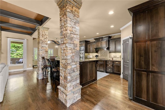 kitchen with crown molding, dark brown cabinets, decorative columns, and dark wood-style flooring