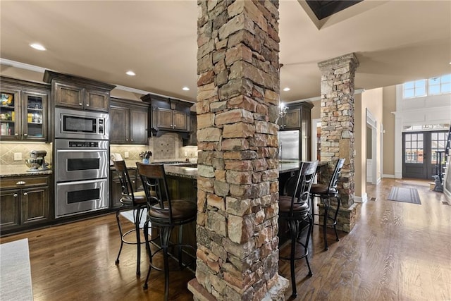kitchen with ornamental molding, decorative columns, a breakfast bar, and stainless steel appliances