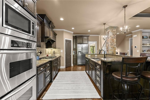 kitchen featuring crown molding, a sink, stone countertops, stainless steel appliances, and a kitchen bar