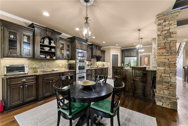 dining room featuring a toaster, a chandelier, ornamental molding, ornate columns, and dark wood-type flooring