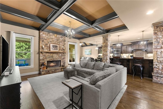living room with a fireplace, ornate columns, dark wood-style floors, and a chandelier