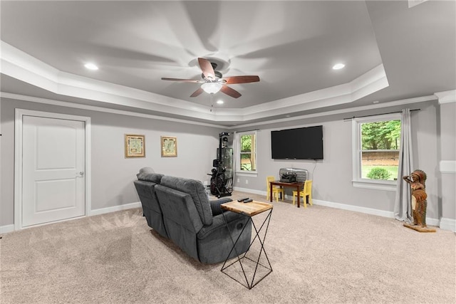 living area with a tray ceiling, light colored carpet, a healthy amount of sunlight, and ceiling fan
