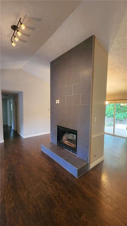 unfurnished living room featuring a textured ceiling, vaulted ceiling, wood finished floors, and baseboards