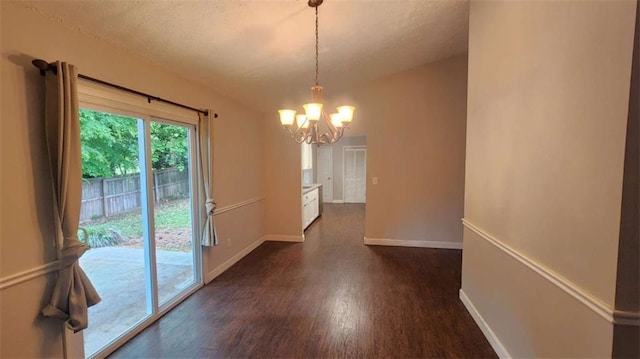 unfurnished dining area with dark wood-type flooring, a chandelier, a textured ceiling, and baseboards
