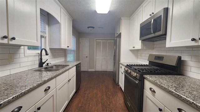 kitchen featuring a sink, dark wood-type flooring, light stone counters, white cabinets, and appliances with stainless steel finishes
