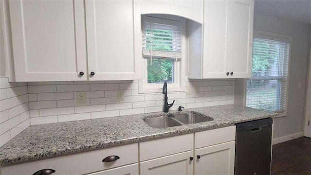 kitchen with black dishwasher, a sink, white cabinets, and baseboards