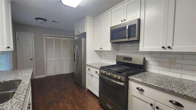 kitchen with appliances with stainless steel finishes, dark wood-style flooring, decorative backsplash, and white cabinets
