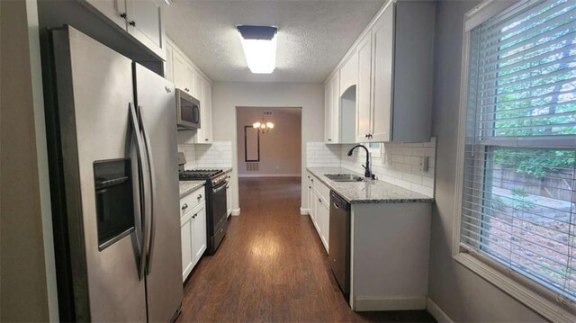 kitchen with decorative backsplash, a sink, stainless steel appliances, dark wood-style floors, and light stone countertops
