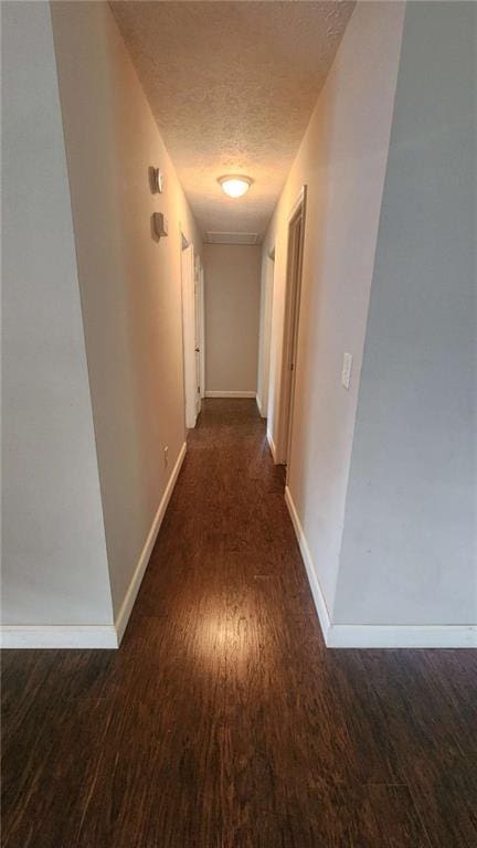 hallway featuring baseboards, wood finished floors, and a textured ceiling