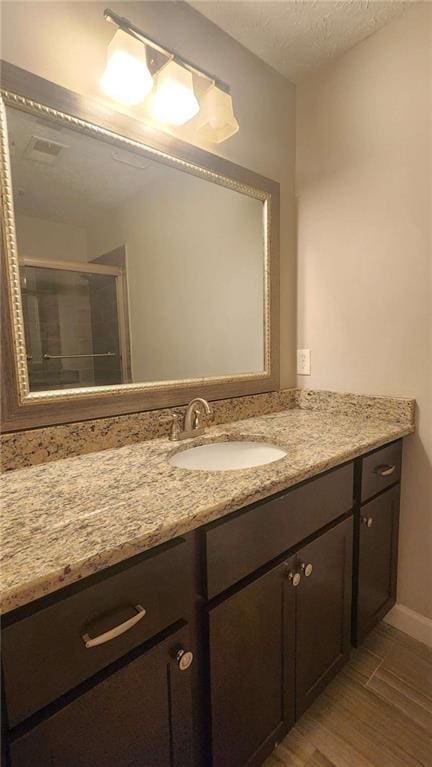 bathroom featuring vanity, a shower with shower door, baseboards, a textured ceiling, and wood finished floors