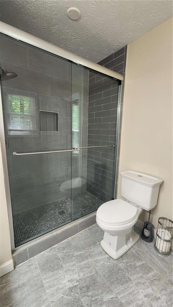 bathroom featuring toilet, a stall shower, a textured ceiling, baseboards, and tile patterned flooring