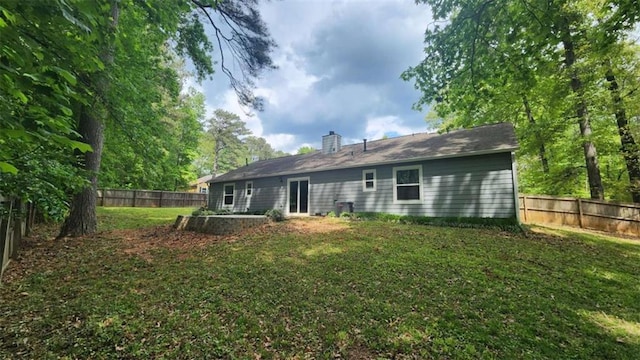 back of house featuring a chimney, a fenced backyard, and a lawn