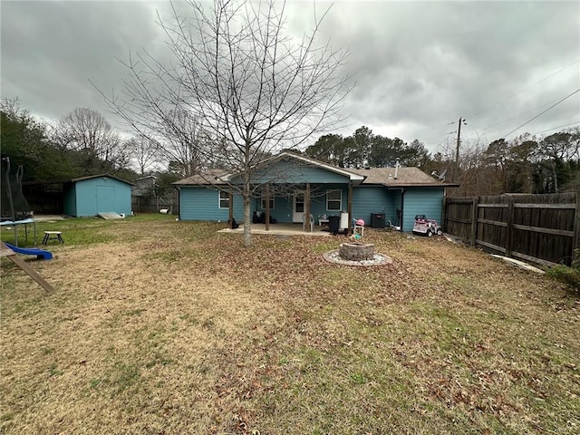 rear view of house with a lawn, a trampoline, a storage shed, central AC unit, and a patio area